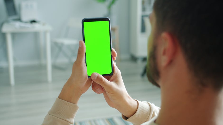 Man holding smartphone with green screen for mockup application indoors.