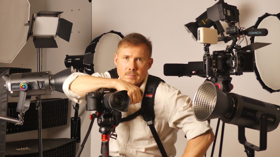 Photographer in a studio surrounded by professional cameras and lighting gear.