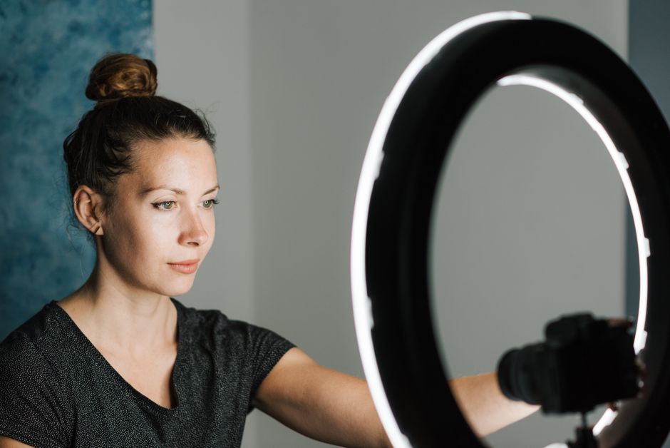 Young female in casual T shirt taking selfie with digital photo camera near professional studio lamp
