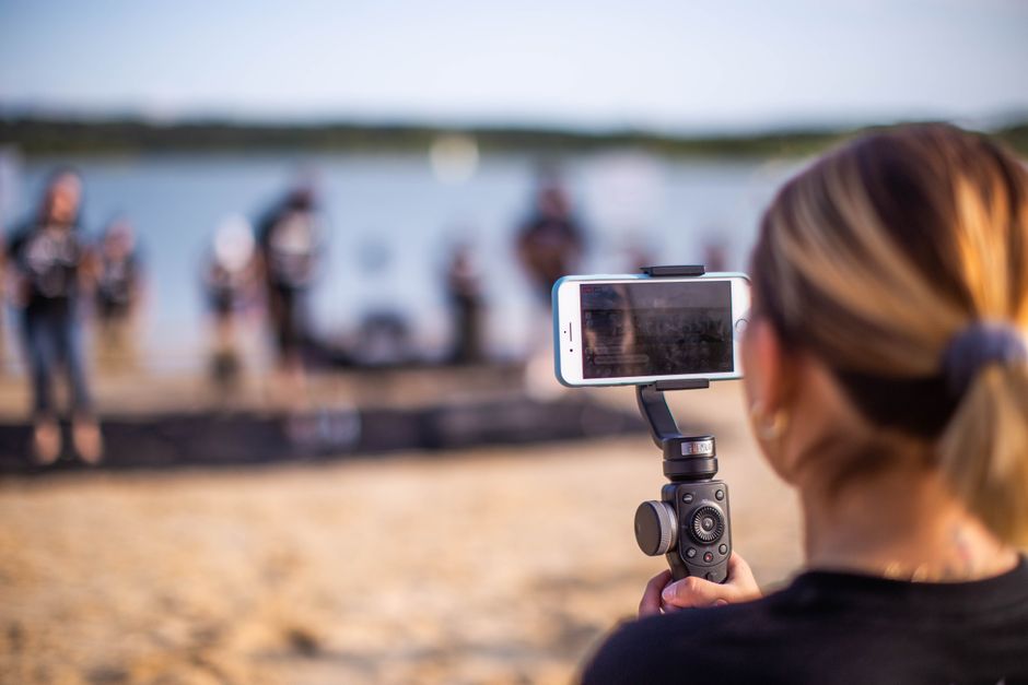 Unrecognizable female using smartphone to record video of band during music show on beach