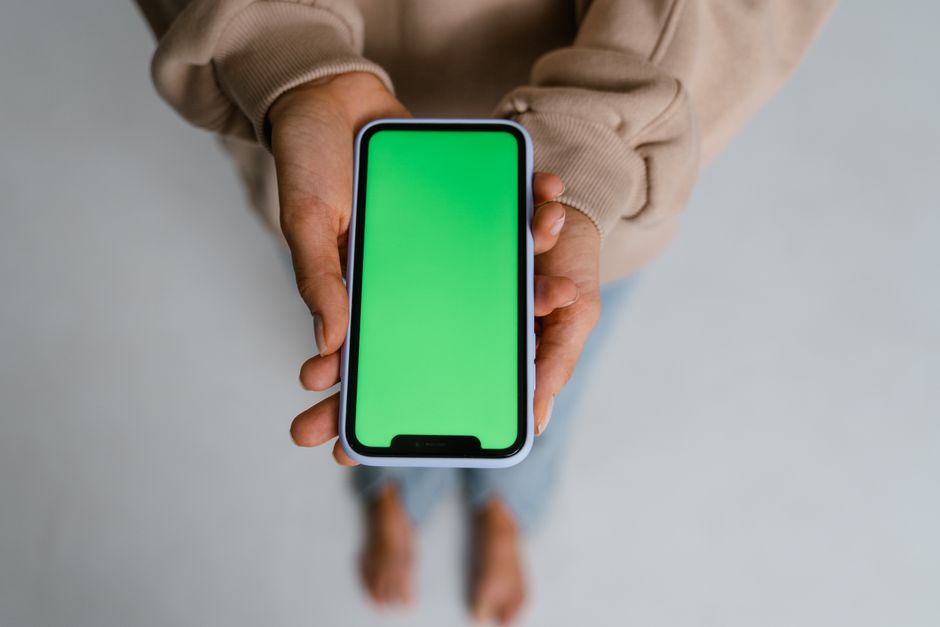 Close-up of a person holding a smartphone with a green screen background, perfect for digital content overlays.