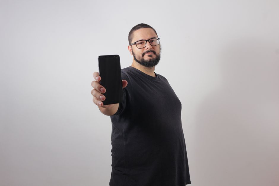 Man presenting a smartphone with a blank screen against a white background.
