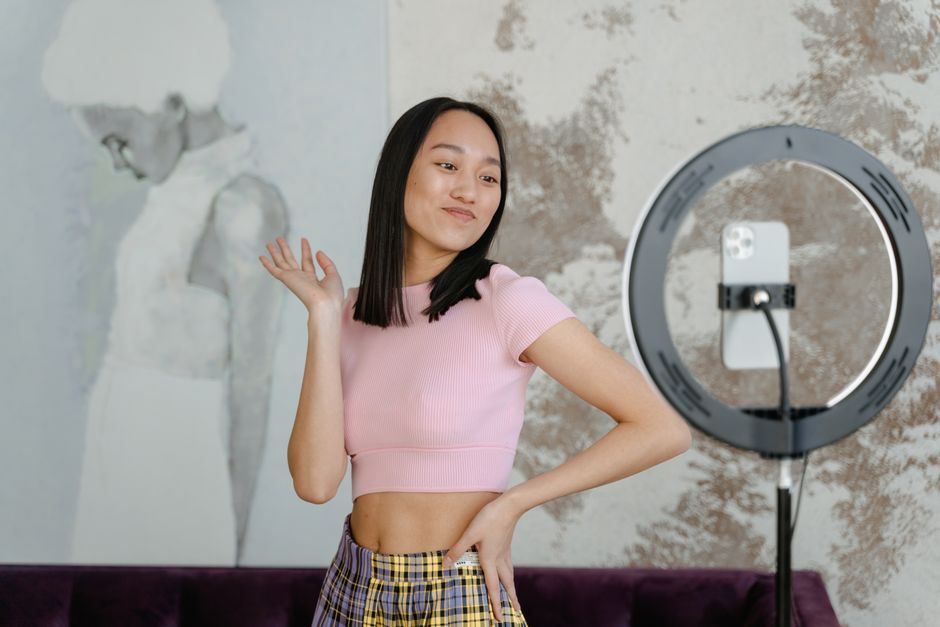 A young woman recording a dance video for social media with her smartphone indoors.