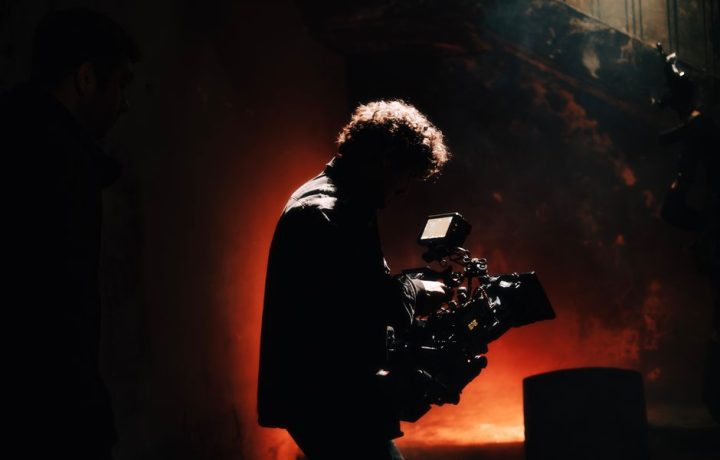A professional cameraman captures footage in a creatively lit, moody setting, backlit by warm light.