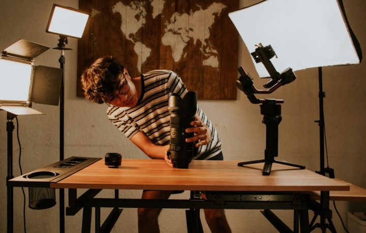 Young man adjusting camera gear in a home studio with soft lighting.