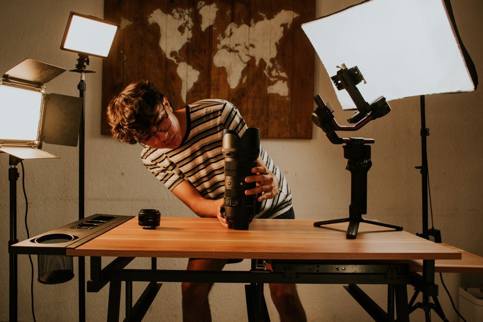 Young man adjusting camera gear in a home studio with soft lighting.