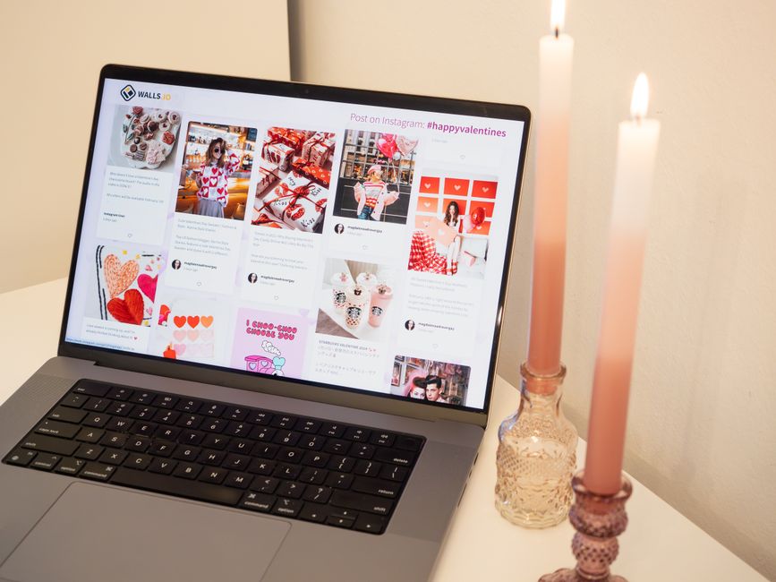 A romantic setup featuring a laptop with Valentine's posts and pink candles, perfect for a cozy atmosphere.