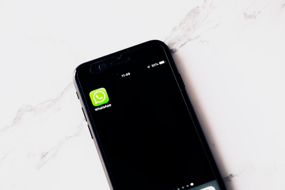 Close-up image of a smartphone displaying WhatsApp on a white table.