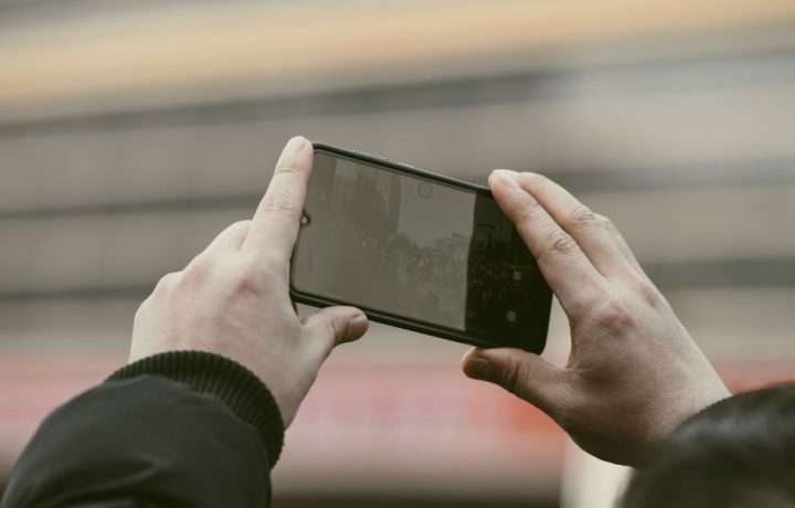 Close-up of hands using a smartphone to capture a photo outdoors.