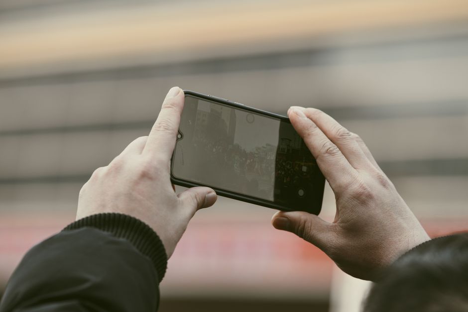 Close-up of hands using a smartphone to capture a photo outdoors.