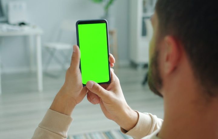Man holding smartphone with green screen for mockup application indoors.
