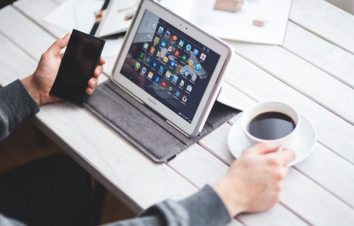 Person using a tablet and smartphone at a table with coffee, showcasing a digital workspace.