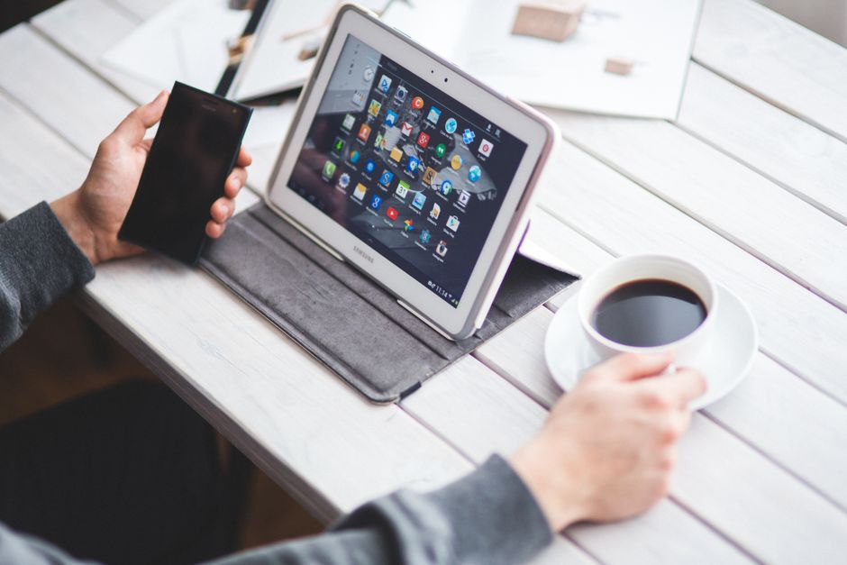 Person using a tablet and smartphone at a table with coffee, showcasing a digital workspace.