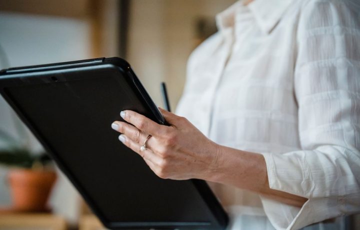 Close-up of a woman holding a digital tablet in an office environment, focusing on hand details.