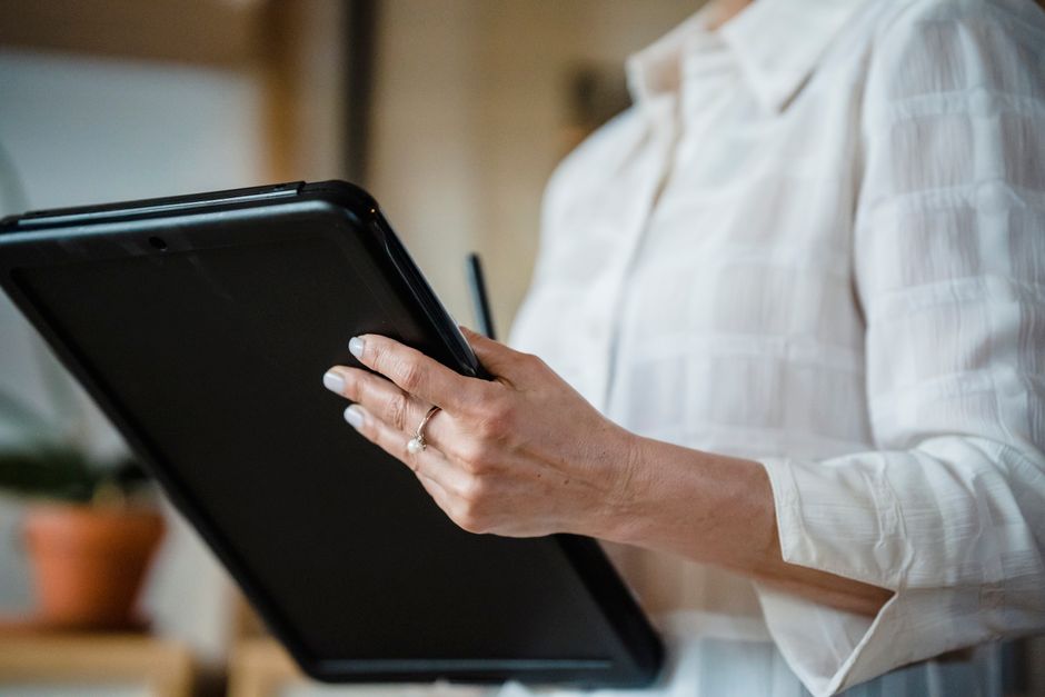 Close-up of a woman holding a digital tablet in an office environment, focusing on hand details.
