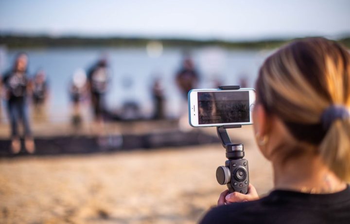 Unrecognizable female using smartphone to record video of band during music show on beach