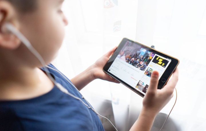 Child holding a tablet indoors, watching videos with headphones, showcasing technology usage by kids.