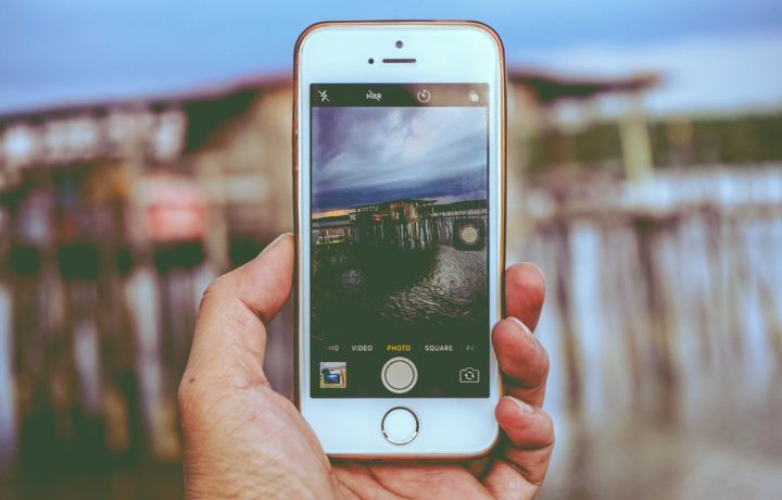 Hand holding smartphone capturing a waterfront scene, showcasing modern mobile technology.