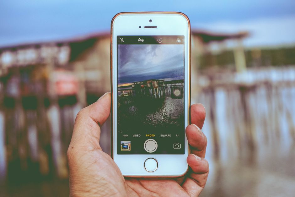 Hand holding smartphone capturing a waterfront scene, showcasing modern mobile technology.