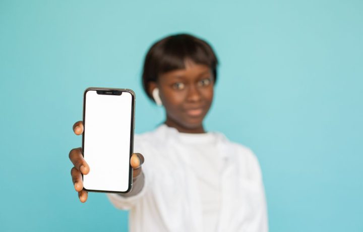 Portrait of a young woman holding a smartphone with a blank screen against a blue background.
