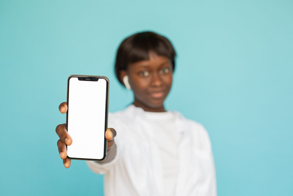 Portrait of a young woman holding a smartphone with a blank screen against a blue background.