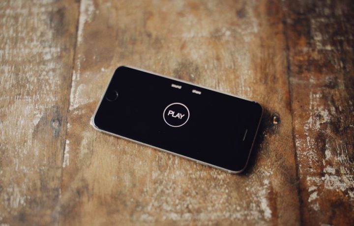 Close-up of a smartphone on a wooden table showing a play icon on its screen.