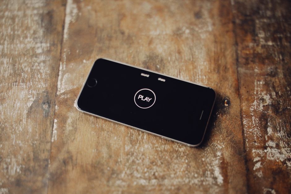 Close-up of a smartphone on a wooden table showing a play icon on its screen.