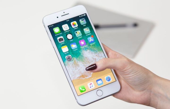 Close-up of a woman's hand holding a smartphone with app icons visible on the screen.