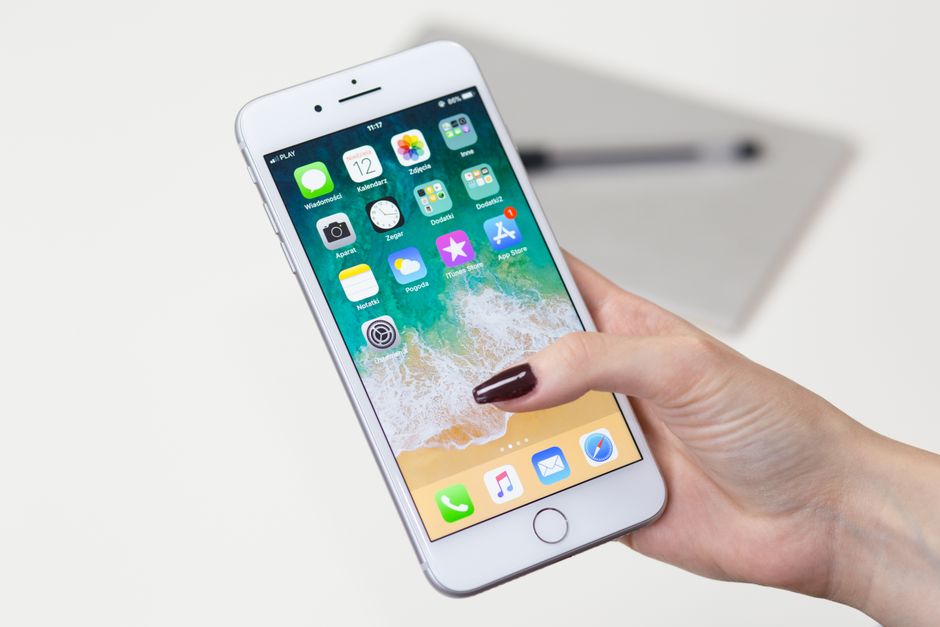 Close-up of a woman's hand holding a smartphone with app icons visible on the screen.