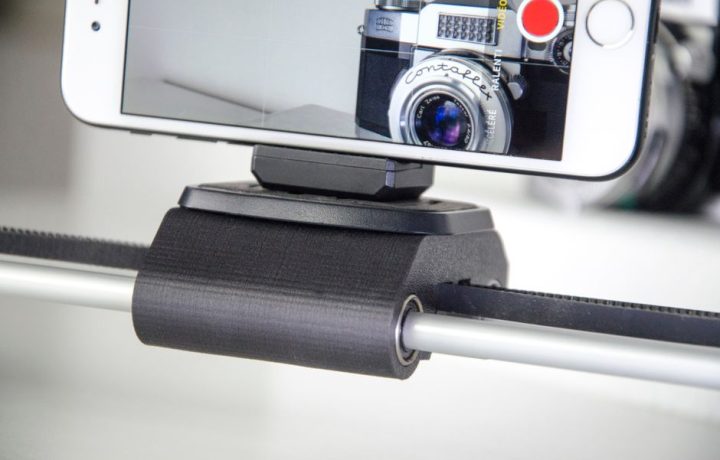 Smartphone capturing video on a slider with a vintage camera in view.