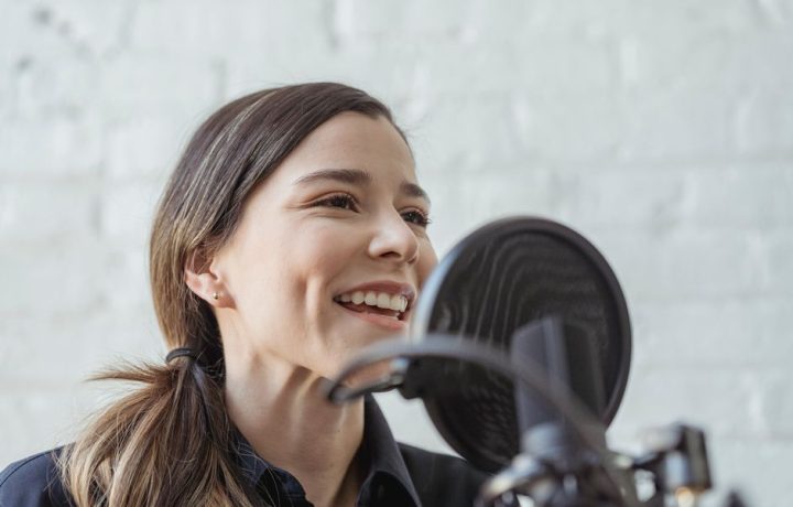 Positive female recording podcast on mic while working in light studio against white brick wall
