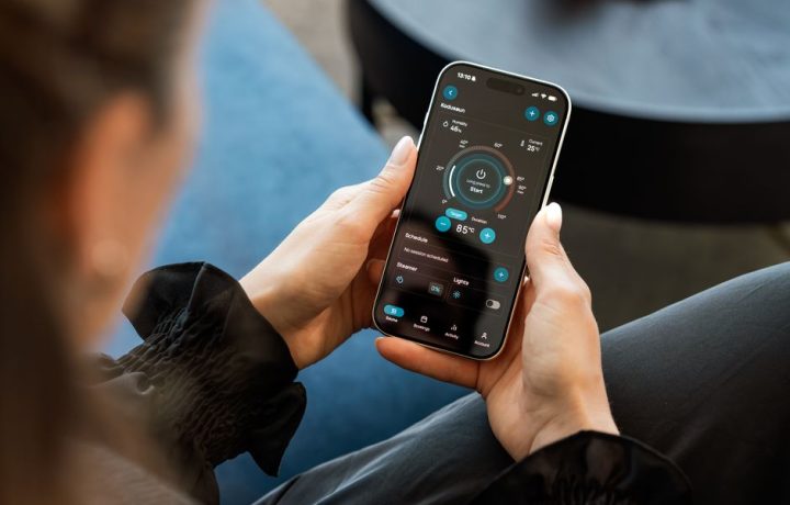 A woman controls a smart sauna system via a touchscreen app on her smartphone indoors.
