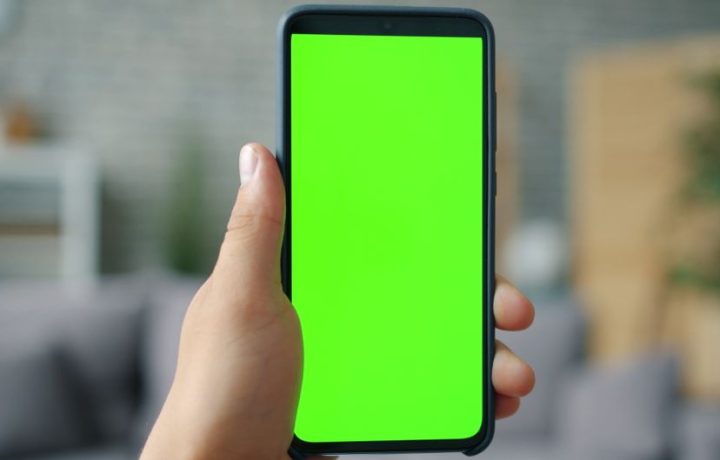 Close-up of hand holding smartphone with green screen, ideal for mockups.
