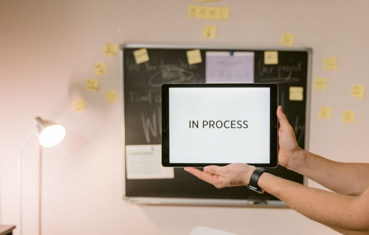 Tablet with 'In Process' text held in an office setting, under analytical review.