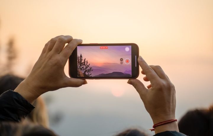 A person capturing a breathtaking sunset on a smartphone, highlighting the blend of technology and nature.