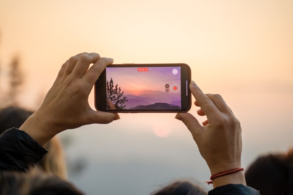 A person capturing a breathtaking sunset on a smartphone, highlighting the blend of technology and nature.