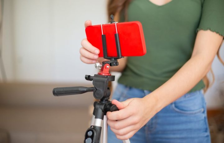 Female adjusting smartphone onto tripod for recording indoors.