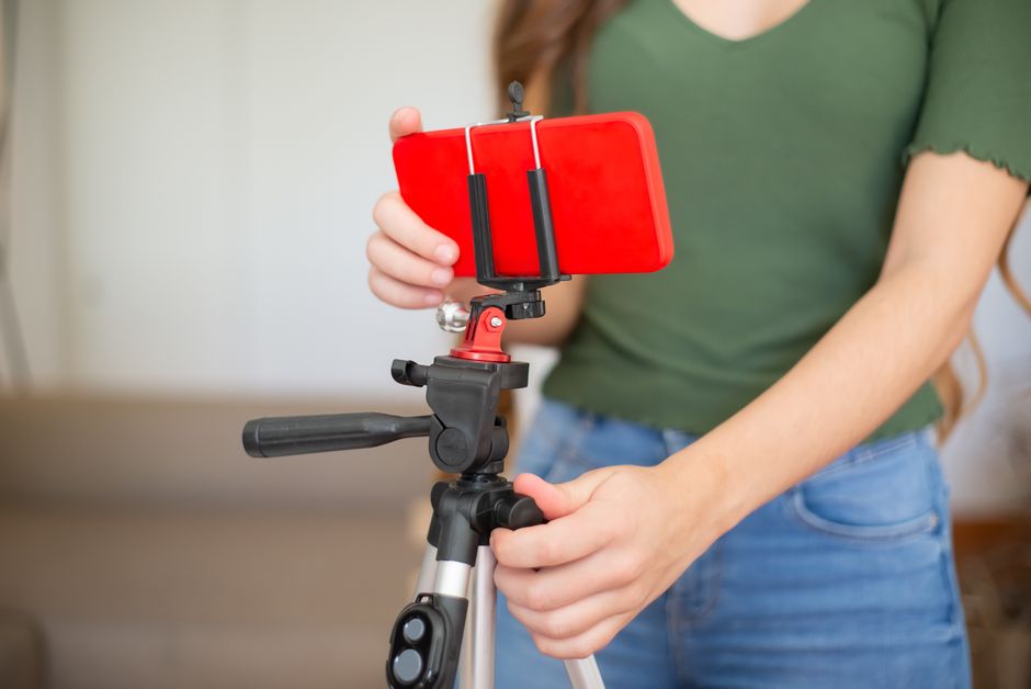 Female adjusting smartphone onto tripod for recording indoors.
