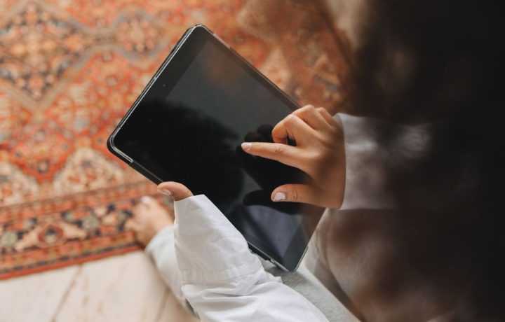 An adult's hands interact with a touch screen tablet placed on a patterned carpet.