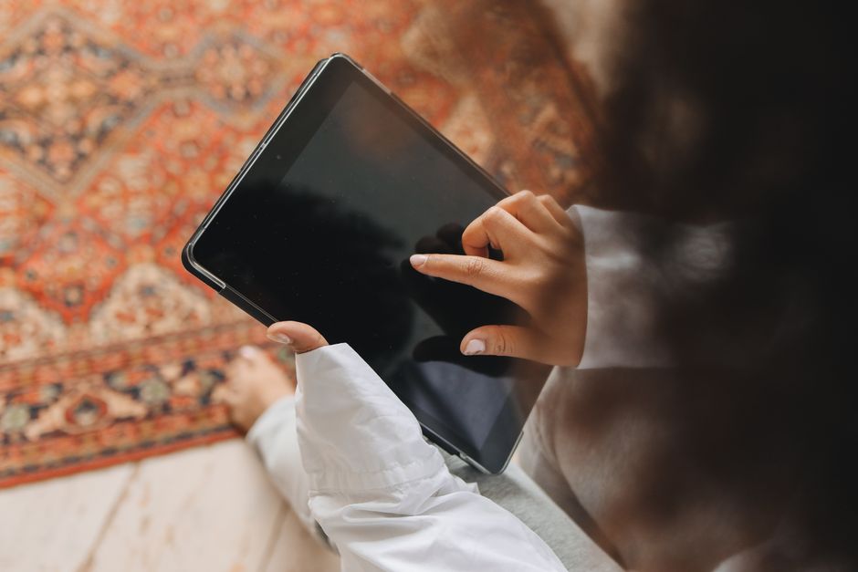 An adult's hands interact with a touch screen tablet placed on a patterned carpet.