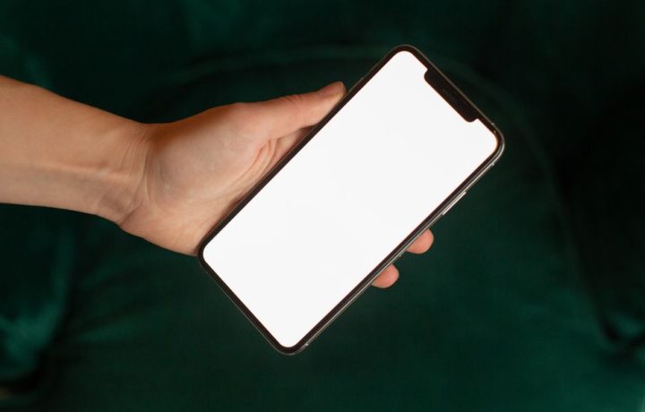 Hand holding a smartphone with a blank screen for mockup purposes.
