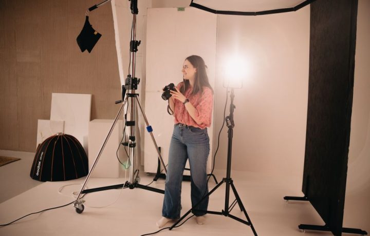 A woman holding a camera during a photoshoot in a well-equipped photo studio.
