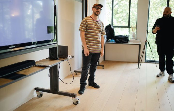 Two men in a casual indoor setting with a large screen, featuring modern technology.