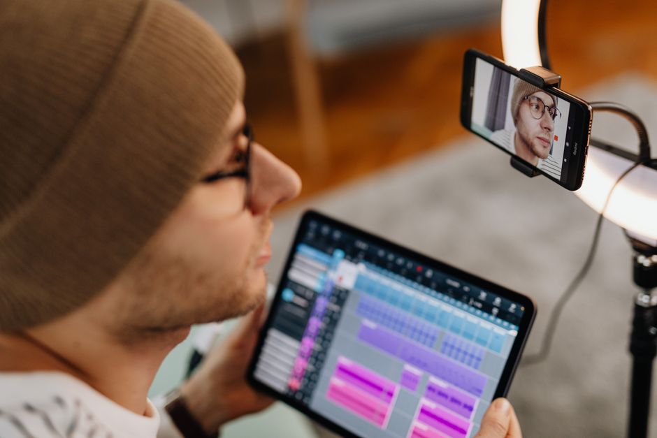 Man with eyeglasses and knitted cap using tablet for video call, illuminated by ring light.