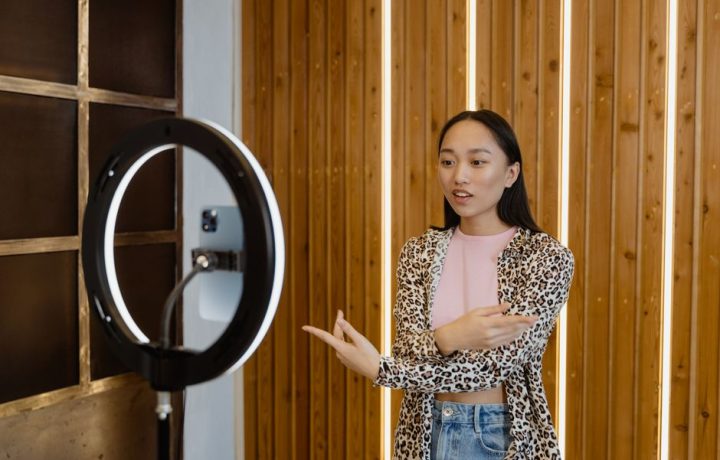 Young Asian woman recording a vlog with a ring light indoors, wearing leopard print.