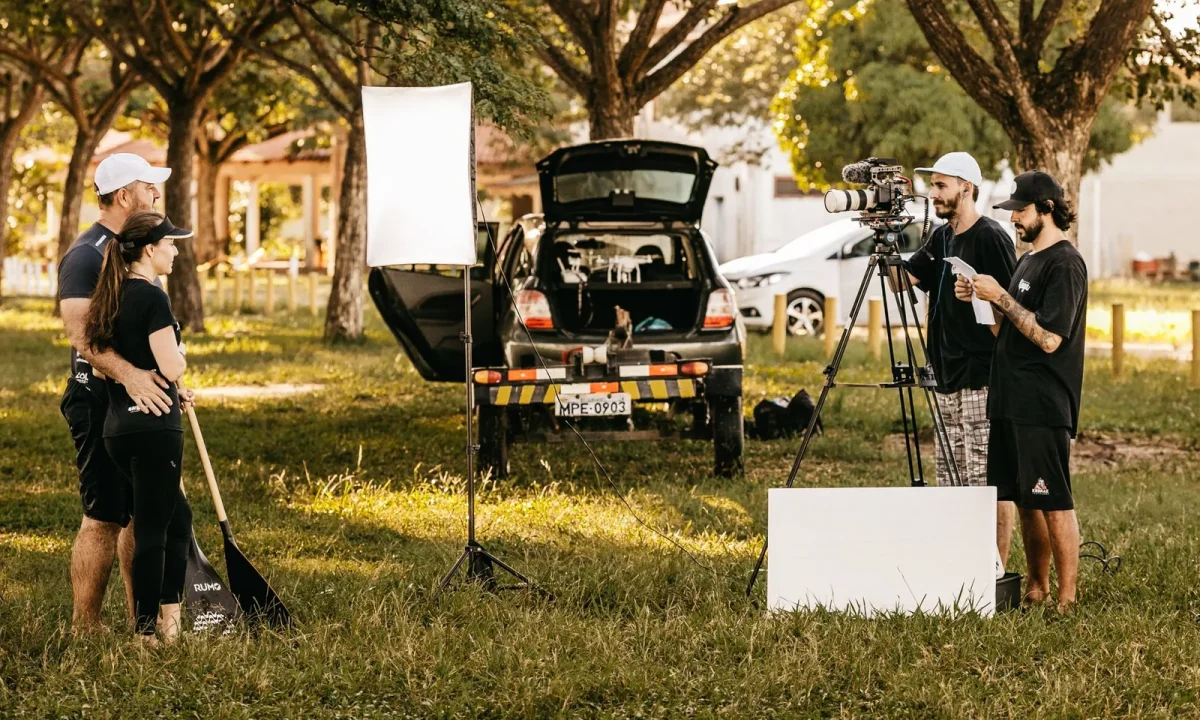 A couple using a teleprompter for interviews while being filmed by camera operators in a park setting