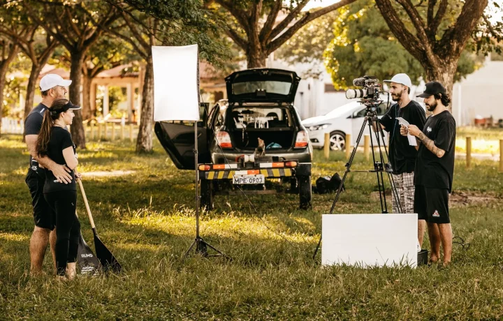 A couple using a teleprompter for interviews while being filmed by camera operators in a park setting
