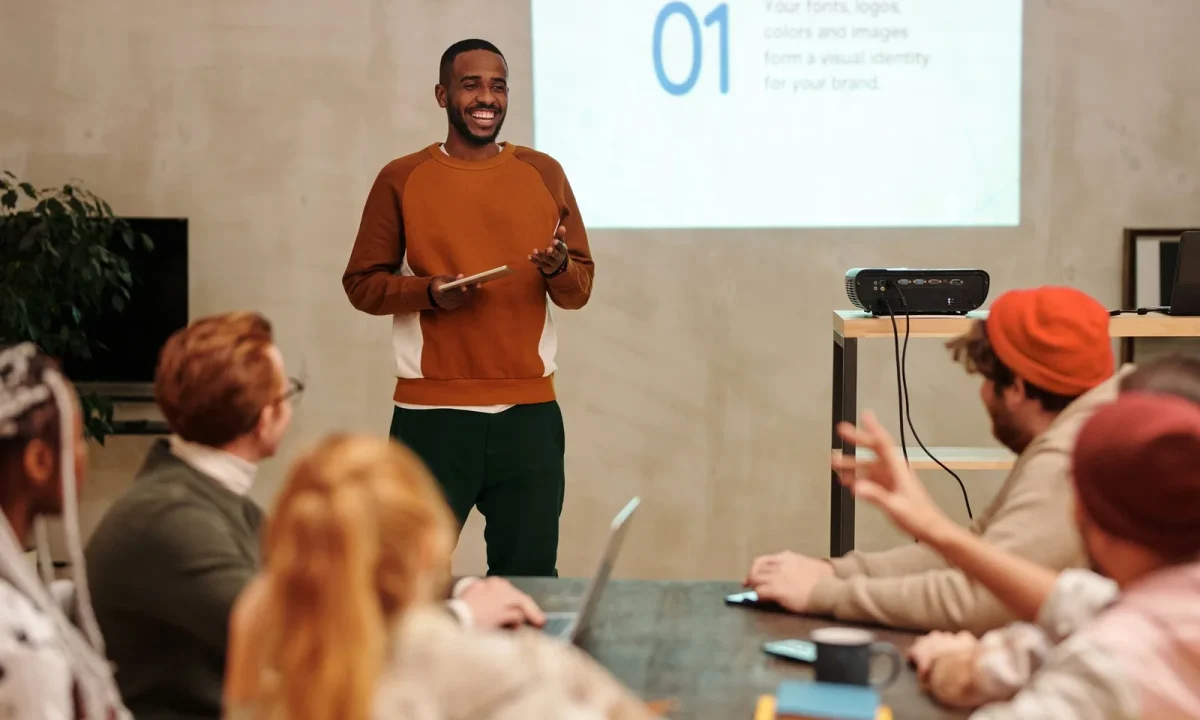 A man confidently presents in a sleek office setting to an engaged and diverse audience