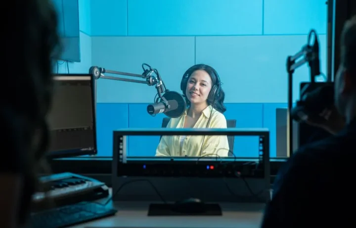 A podcast host records a show in a professional radio studio with microphones and headphones.