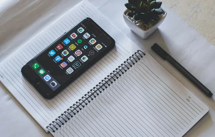 Flat lay with a smartphone on a notebook, showcasing free vs paid teleprompter apps with a plant and pen